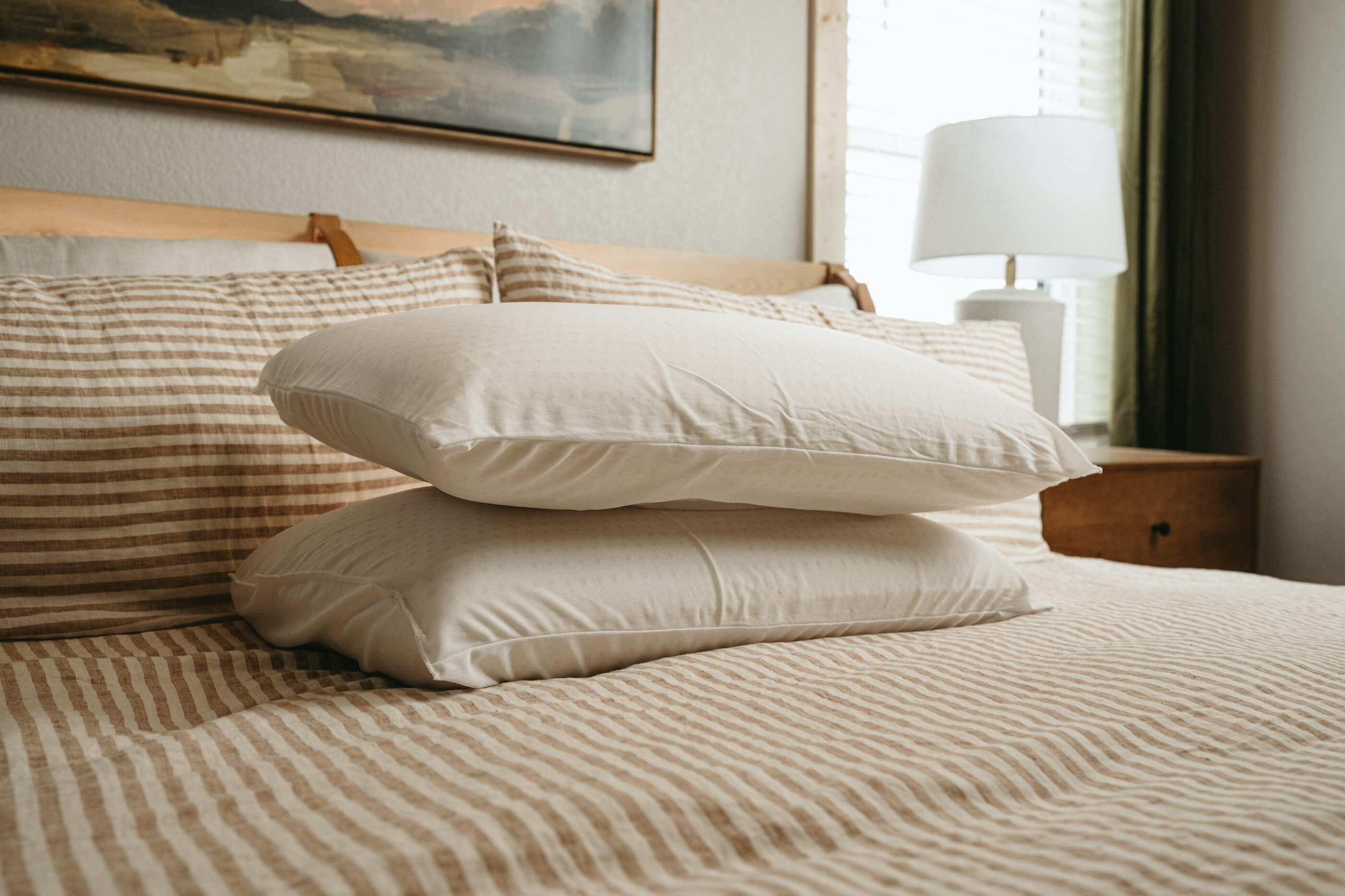 Stitchco pillows stacked on striped linen bedding in a cozy bedroom