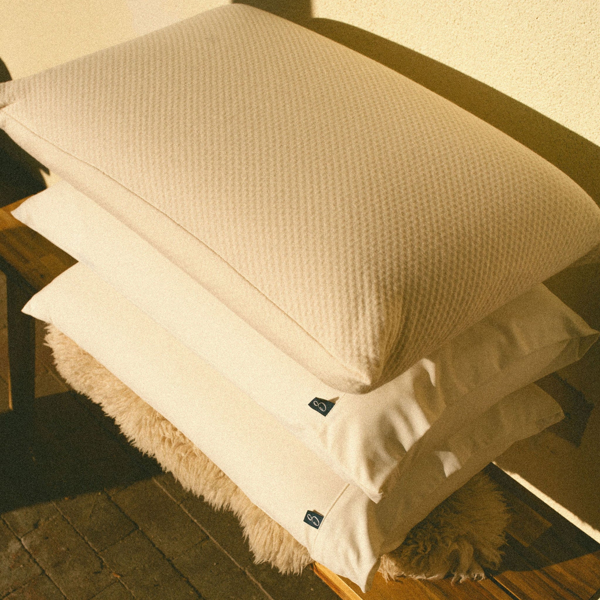 Stack of white pillows on a wooden bench with a textured surface.